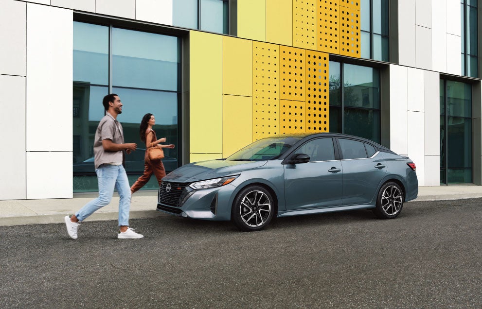 Smiling couple walking towards a parked Nissan Sentra